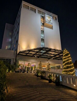 Un hôtel au design moderne, doté d’une entrée imposante avec une allée couverte et décorée de sapins de Noël.