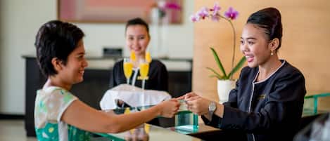 A reception area with a glass counter, a potted plant, and a person handing over a card.