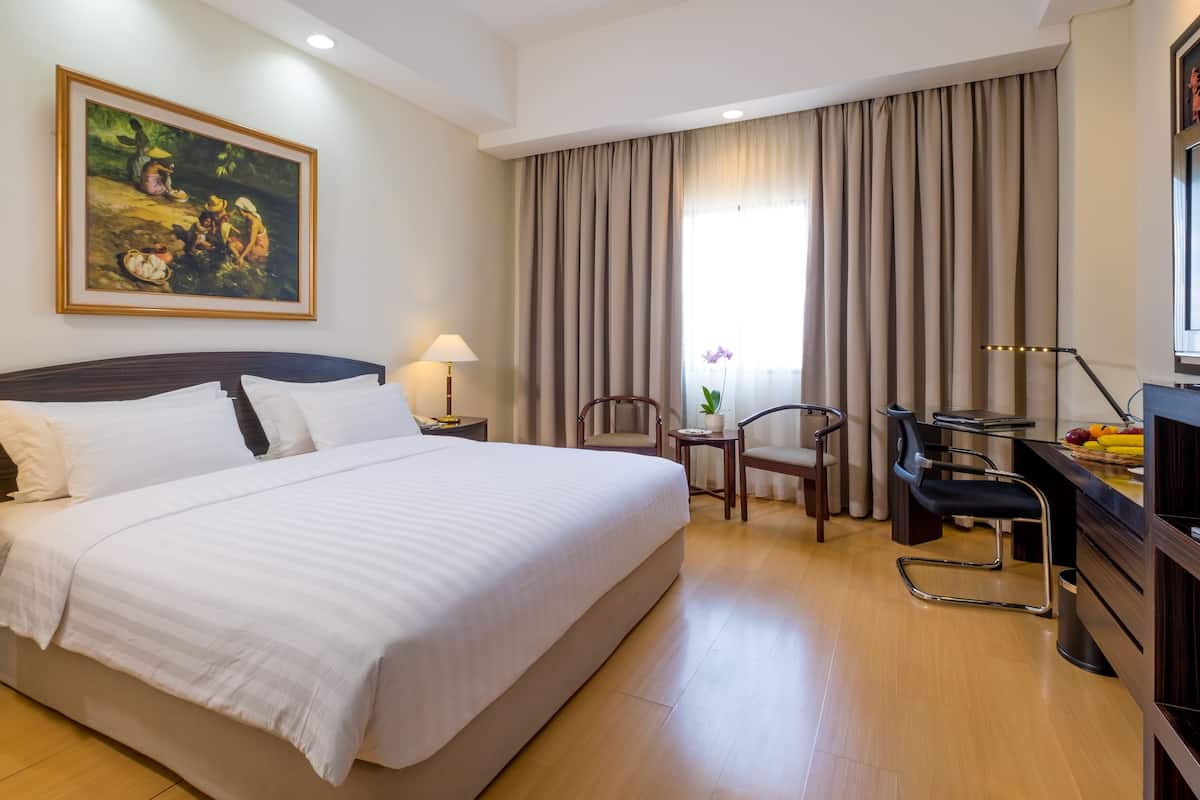 Een hotelkamer met een groot bed, twee nachtkastjes met lampen, een bureau met stoel, een televisie en een schilderij aan de muur.
