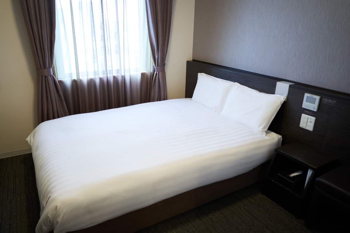 A hotel room with a large bed, a nightstand, and a control panel on the headboard.