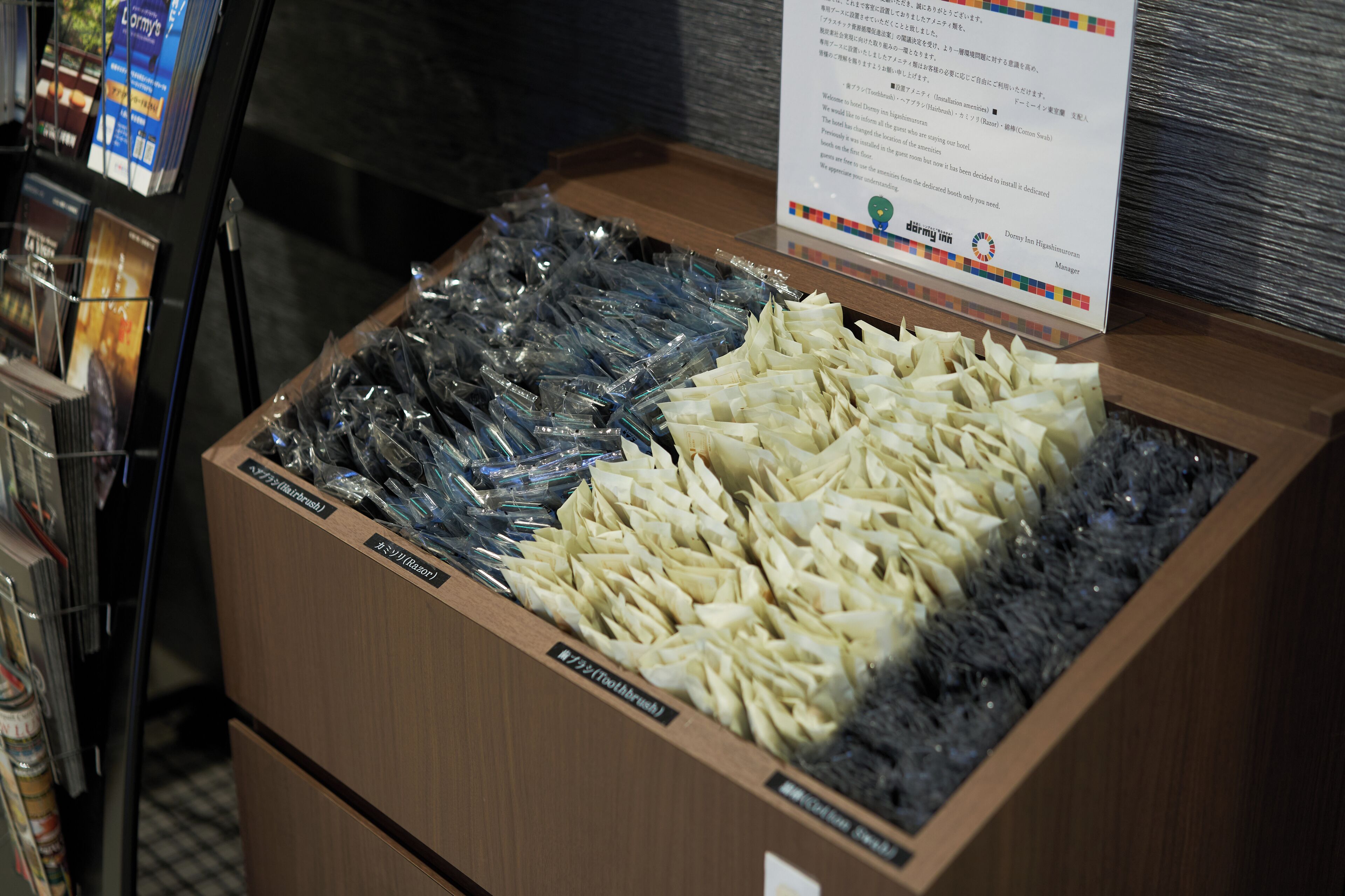 Een display met verpakte producten in een houten doos met labels, naast een tijdschriftenrek.