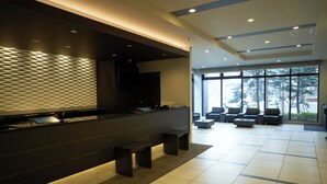 Een moderne lobby met een receptiebalie, een zithoek en grote ramen met uitzicht op het omliggende landschap.