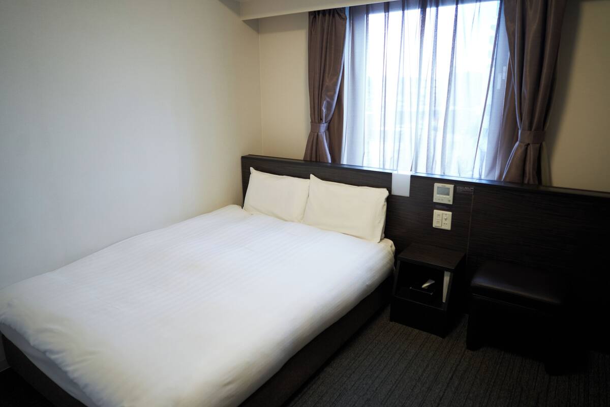 A hotel room with a single bed, a nightstand, a desk, and a window with curtains.
