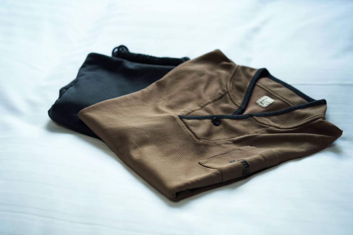Two folded shirts, one black and one brown, on a white surface.