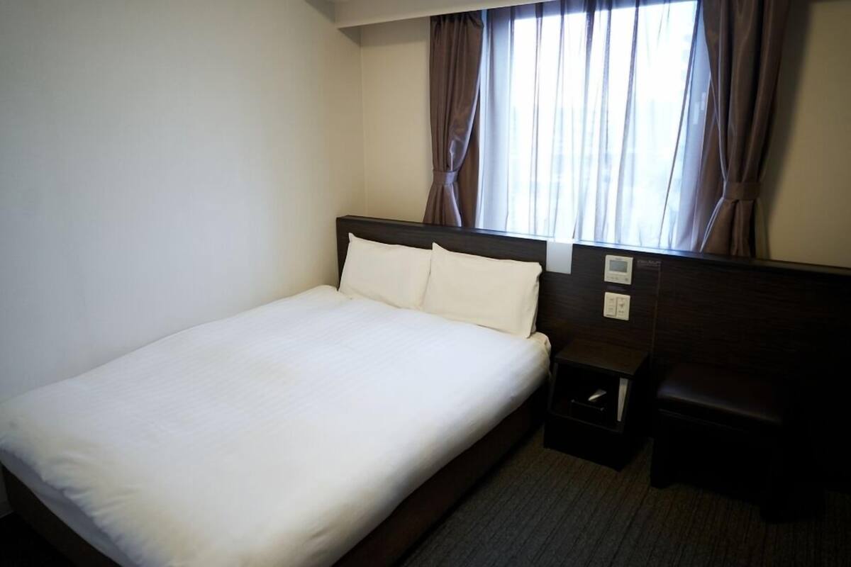 A hotel room with a single bed, a nightstand, a desk, and a window with curtains.