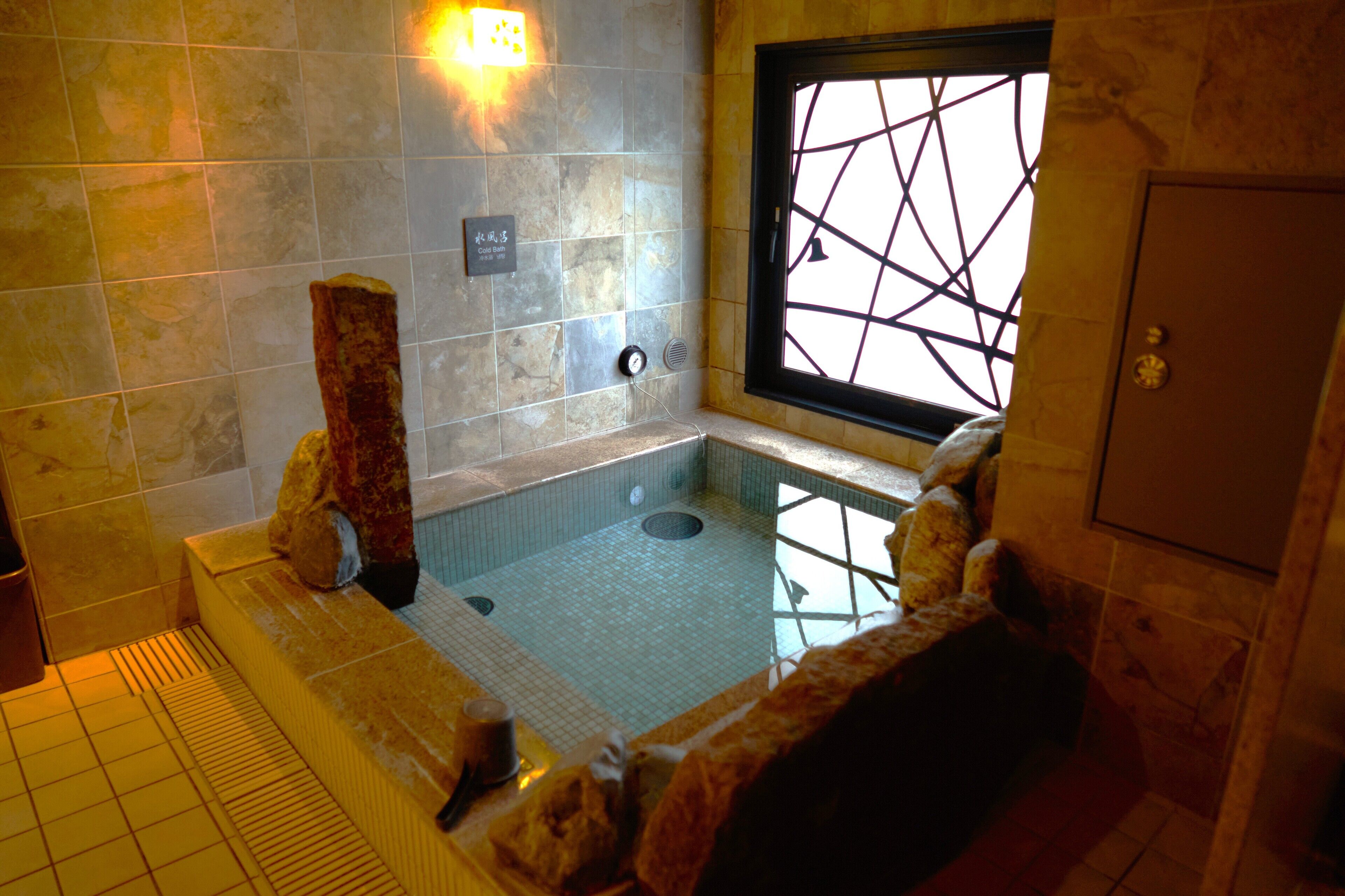 A spa area with a stone wall, a window with a geometric pattern, and a bathtub.
