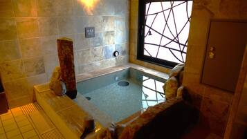 A spa area with a stone wall, a window with a geometric pattern, and a bathtub.