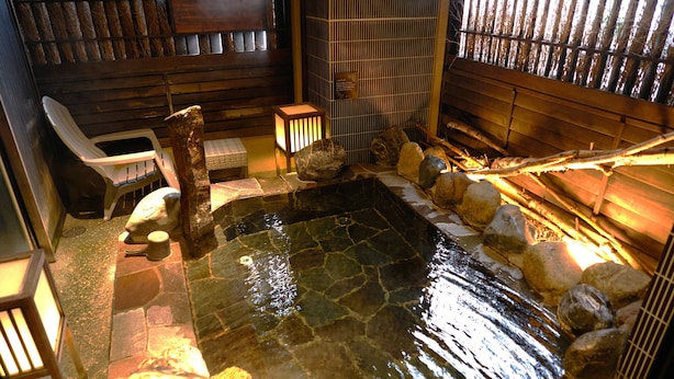 Een traditioneel Japans onsen met een stenen warmwaterbron, houten banken en een bamboebegraaf.
