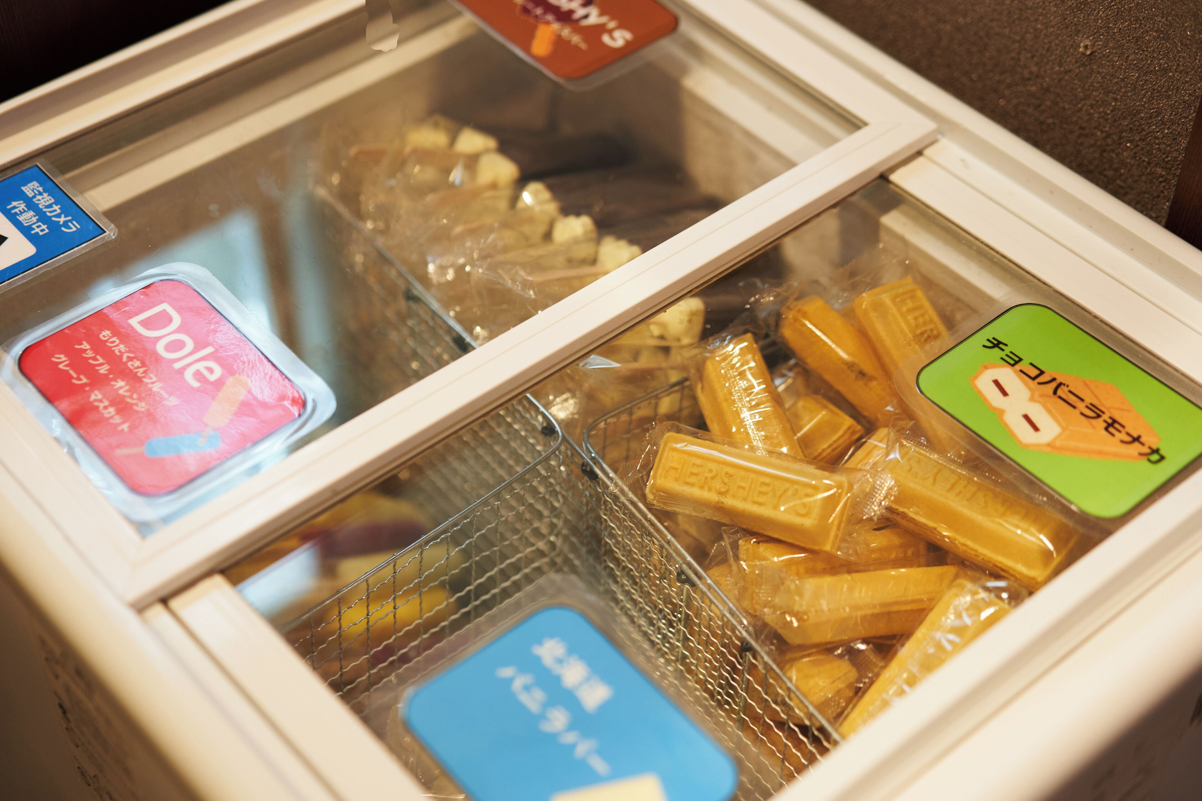 A refrigerated display case with various packaged food items, including a visible Dole brand product and a Hershey's chocolate bar.