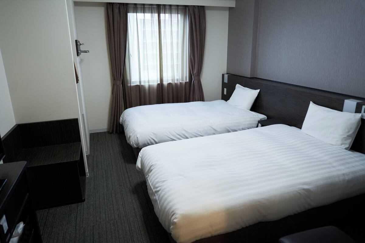 A hotel room with two single beds, a desk, and a window with curtains.