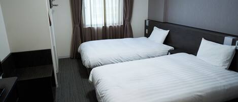 A hotel room with two single beds, a desk, and a window with curtains.