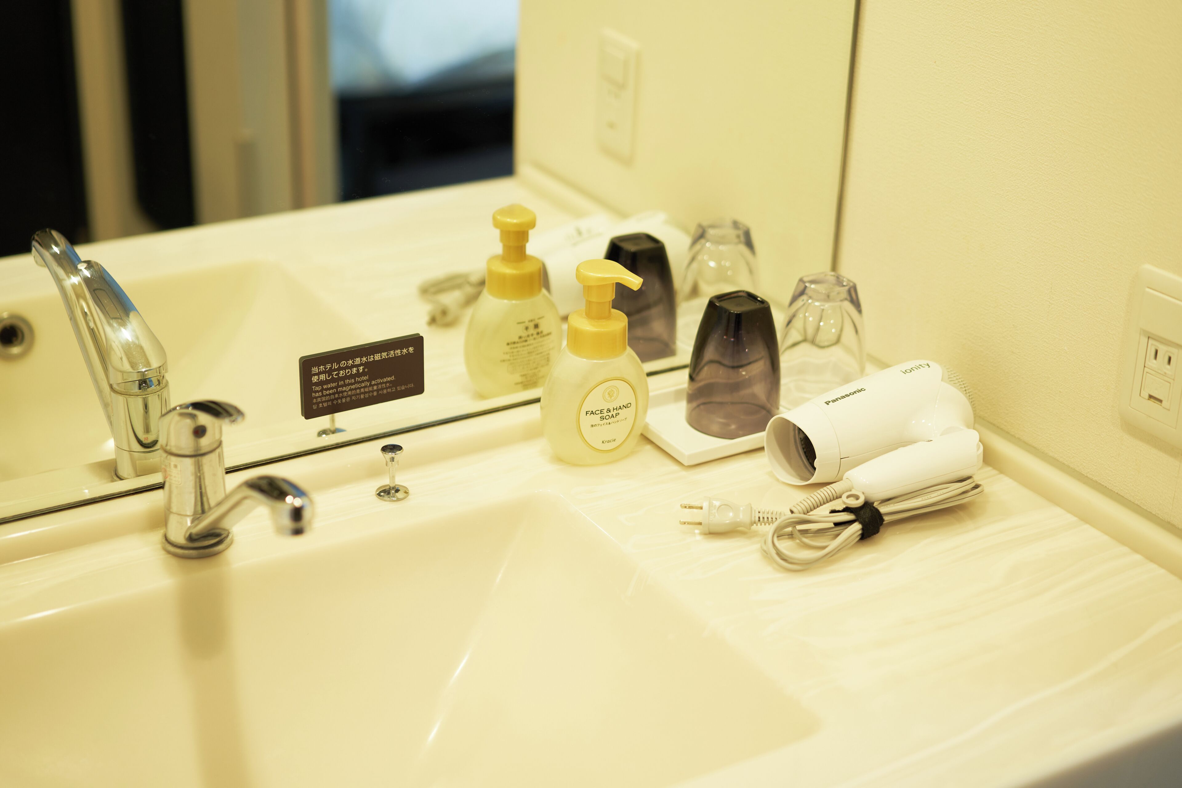 A hotel bathroom with a sink, mirror, toiletries, and a hairdryer.