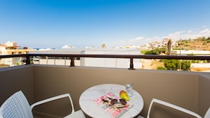 A balcony with a round table, two white chairs, a magazine, a glass of water, and a fruit. - Eltina Hotel (Rethymno)