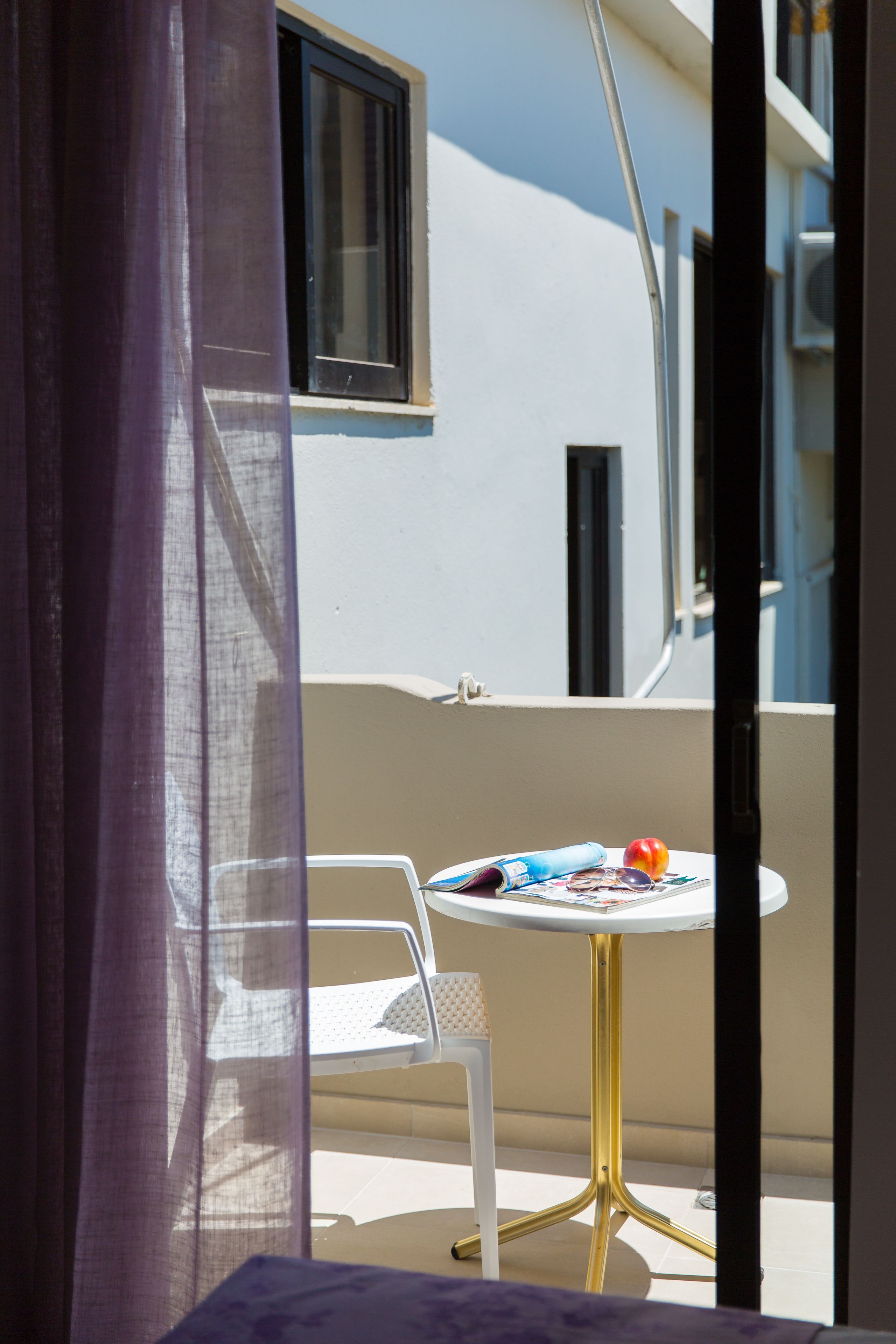 Un balcon avec une chaise blanche et une petite table ronde, une fenêtre et un rideau.