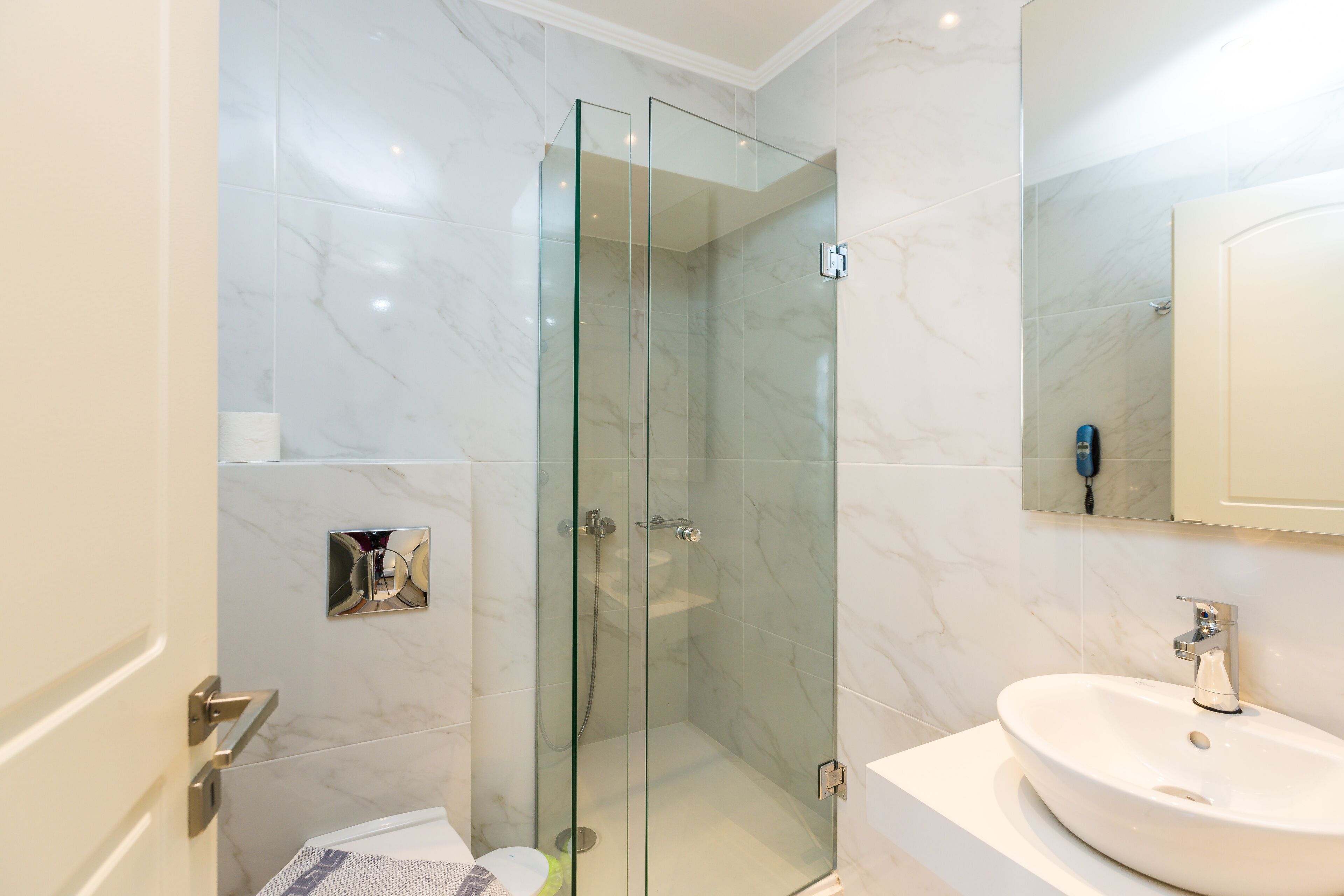 A modern bathroom with a glass-enclosed shower, a white sink, and a marble-tiled wall.
