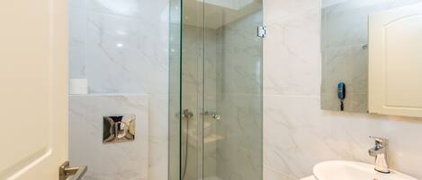 A modern bathroom with a glass-enclosed shower, a white sink, and a marble-tiled wall.