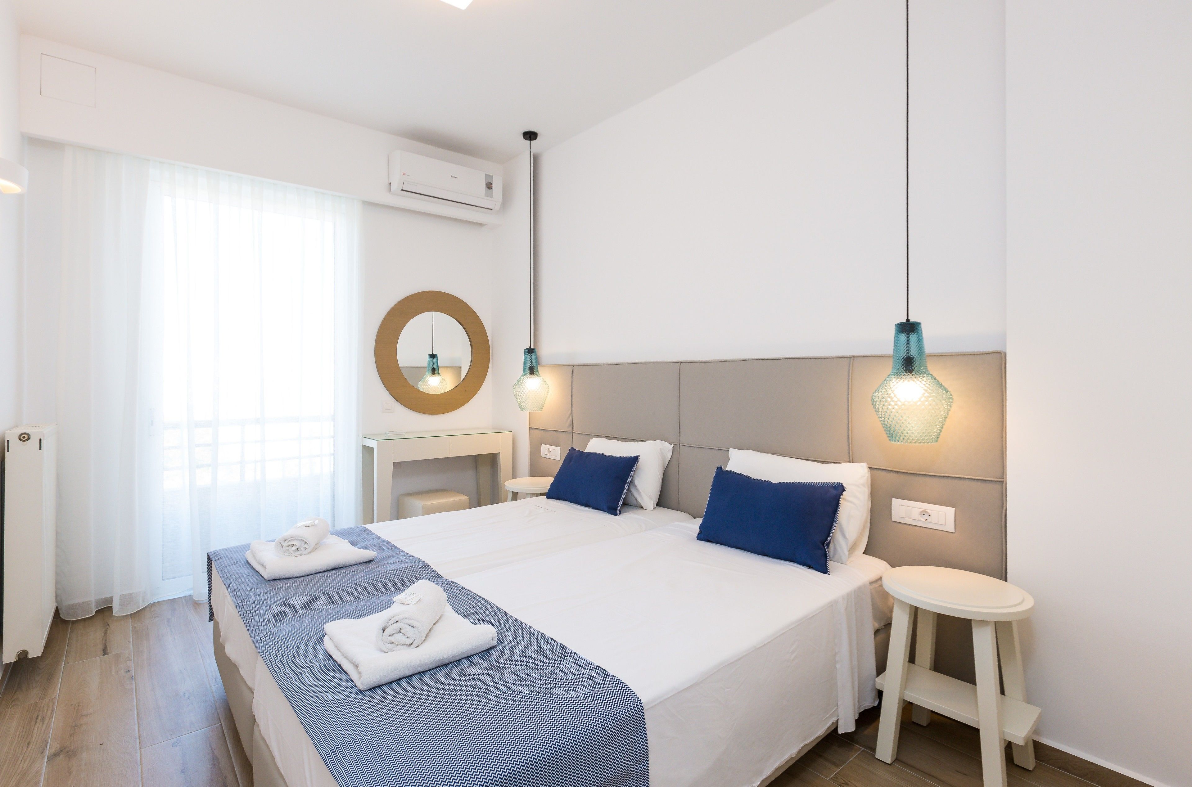 A hotel room with a large bed, two bedside tables, a round mirror, and a small stool.