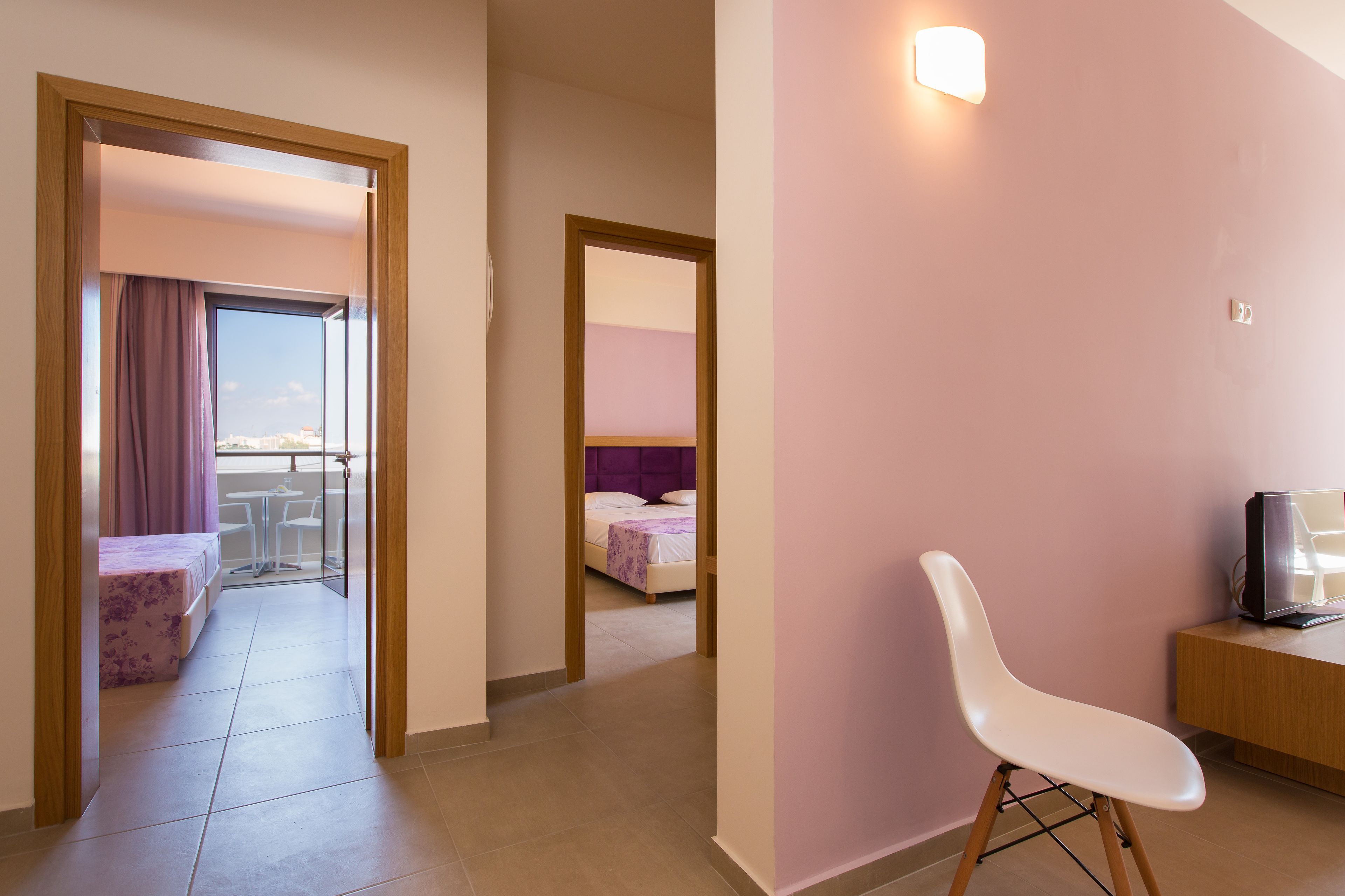A hotel room with a bed, a chair, a TV, and a balcony with a table and chairs.