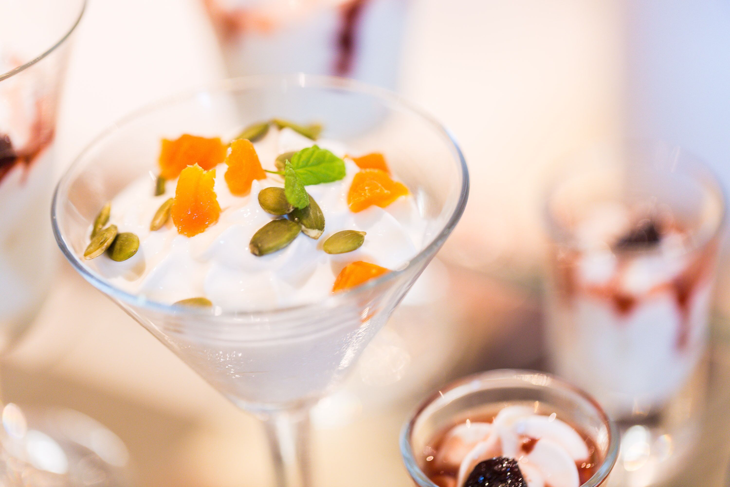 En dessert i ett genomskinligt glas, med vit grädde och bitar av apelsinfrukt, omgiven av andra desserter.