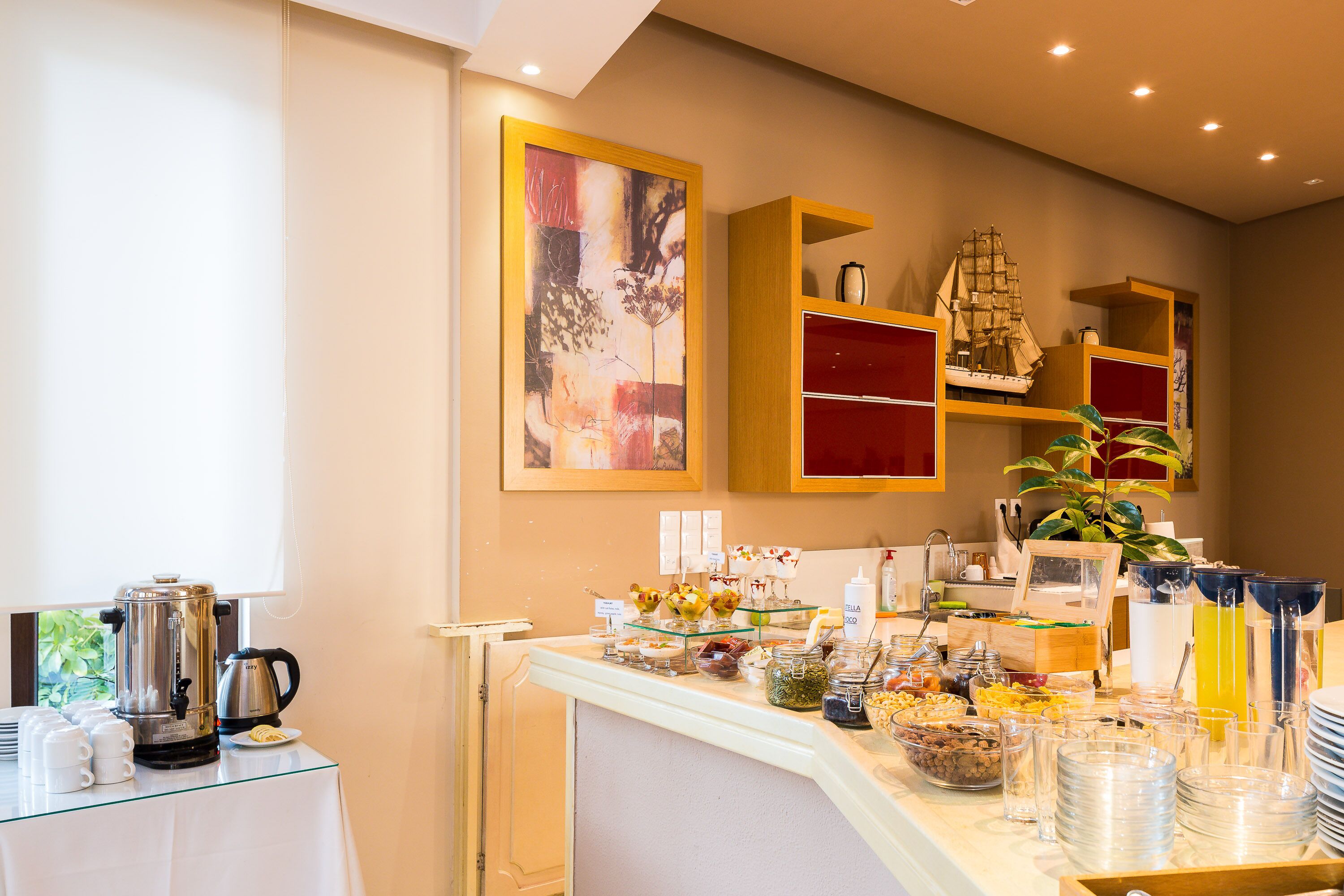Montaje de bufé con diversos alimentos, una estación de café y elementos decorativos como un modelo de barco y arte abstracto.