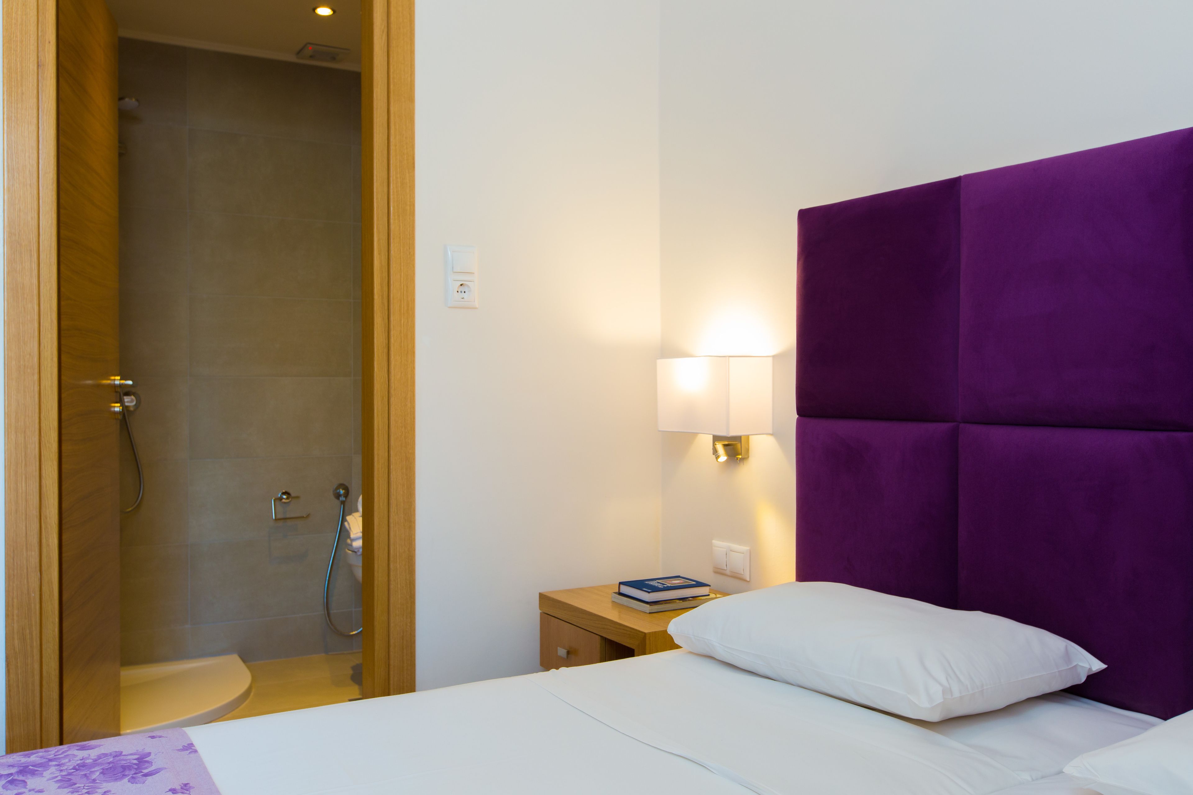 Een hotelkamer met een bed, nachtkastje, lamp, douche en toilet.