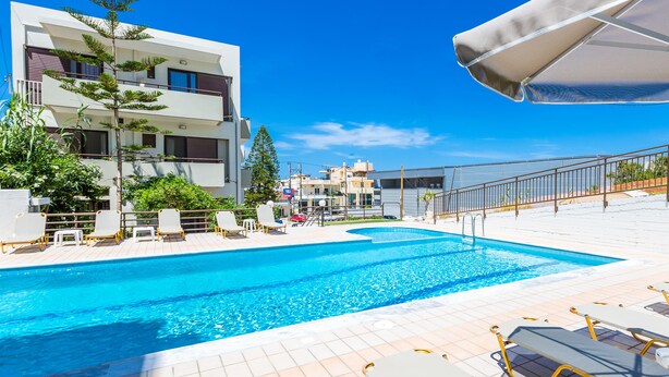 A swimming pool with lounge chairs and a building in the background. - Eltina Hotel (Rethymno)