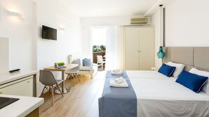 A modern hotel room with a bed, bedside table, and a desk with a chair. There is a TV mounted on the wall and a window with curtains. - Eltina Hotel (Rethymno)