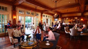 A spacious, elegantly furnished lounge area with high ceilings, large windows, and a bar area with wine bottles.
