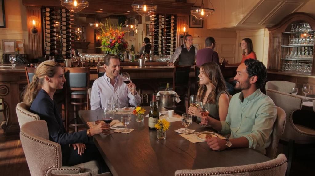A group of people seated around a table in a bar area with a wine rack and bar counter in the background.