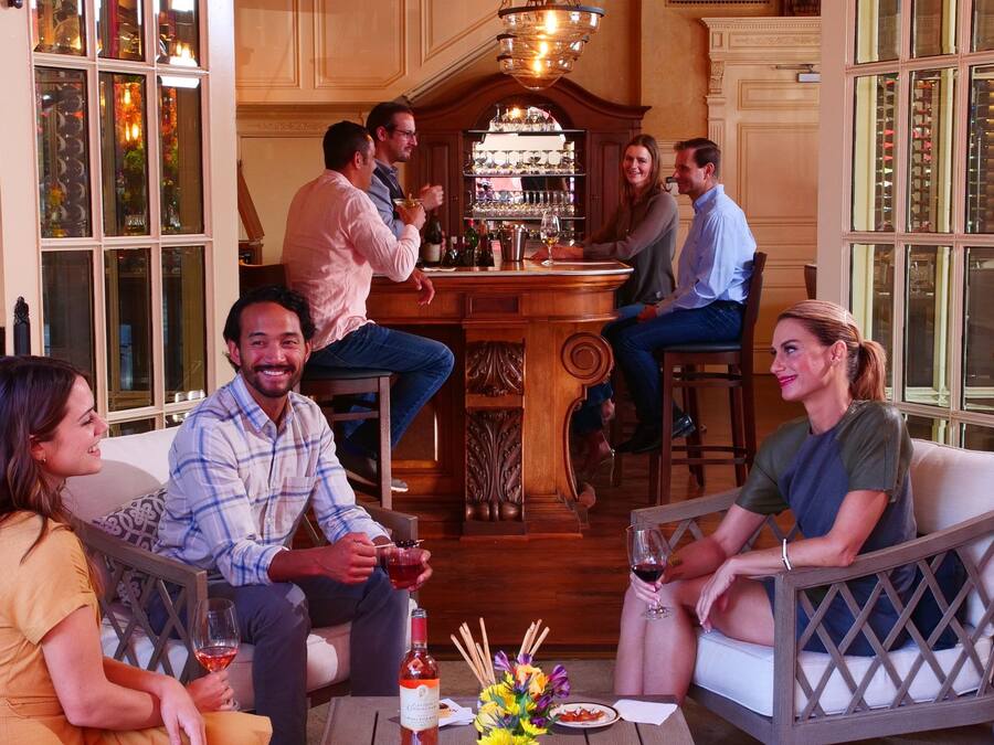 A group of people seated around a bar area with a wine bottle and glasses on the table.