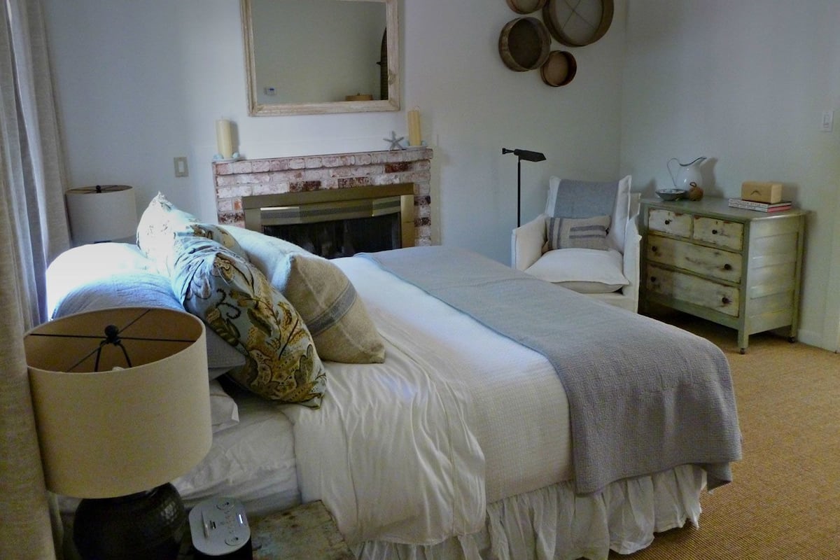 Un dormitorio con cama, cómoda, espejo y chimenea.
