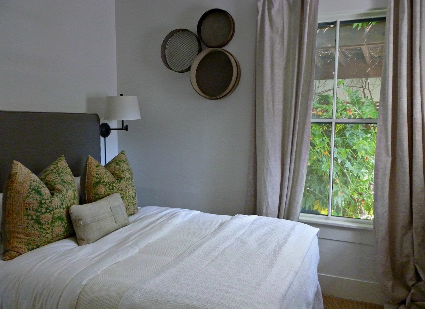 Ein Schlafzimmer mit einem Bett, Kissen, einer Lampe und einem Fenster mit Vorhängen.