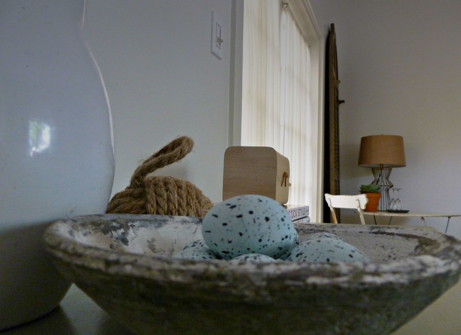 A rustic interior with a stone bowl containing eggs, a rope, and a wooden box.