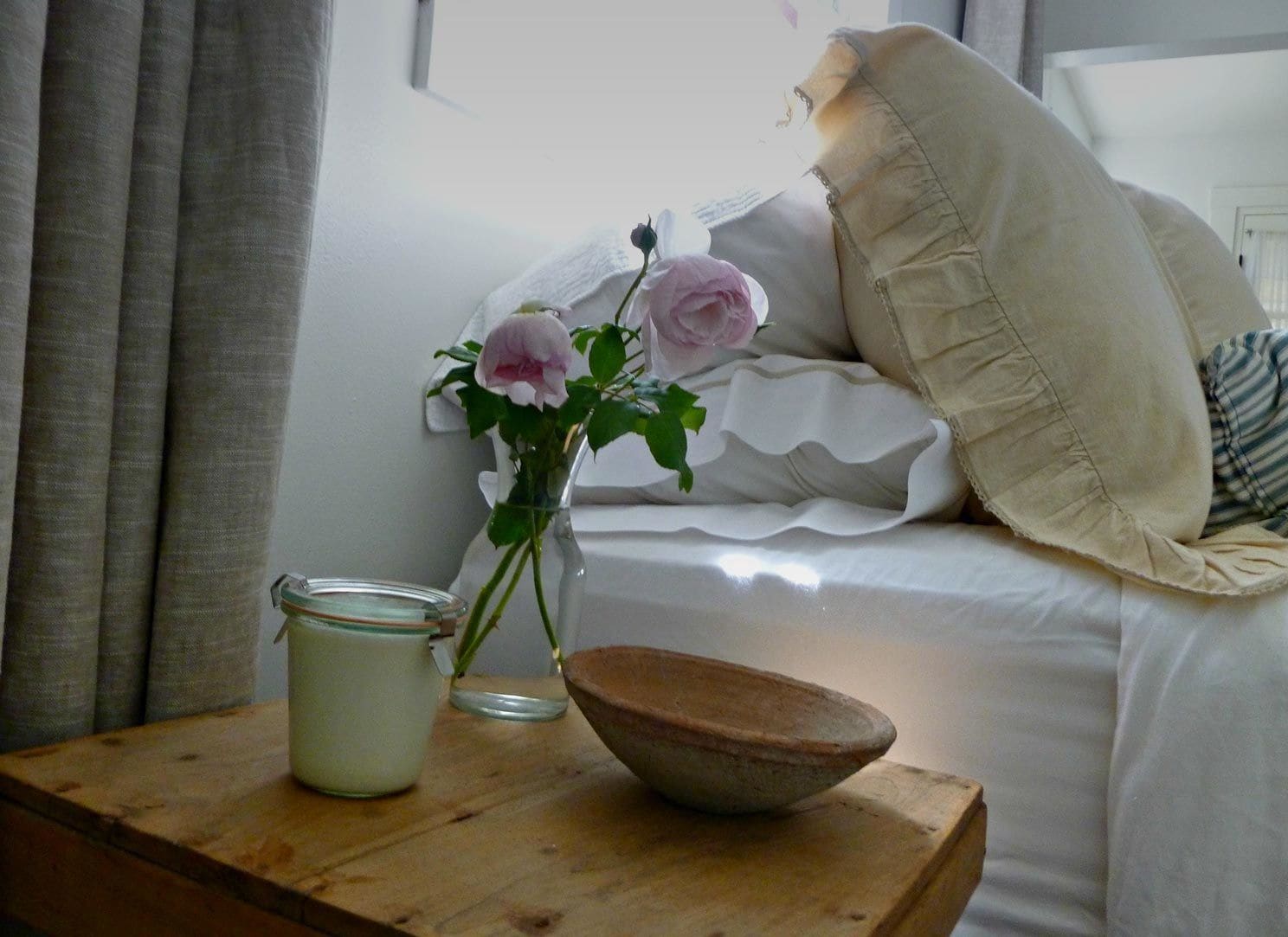 Et soveværelse med en seng, et natbord med en vase blomster, et lys og en skål.