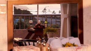 Un balcon avec une table, des chaises, un pot de fleurs et une vue sur l’océan.