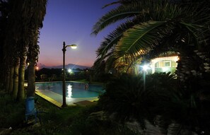 A swimming pool at dusk with a view of a building and mountains in the background. - Dream Castle (Seogwipo)