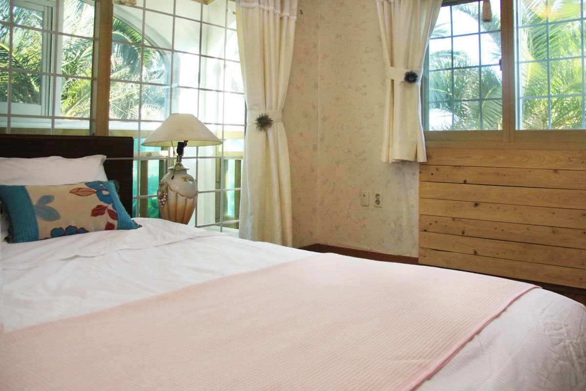 A bedroom with a large bed, a nightstand, a lamp, and a window with curtains.