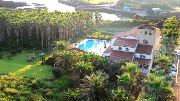 Une grande maison avec une piscine, entourée d’une végétation luxuriante et de palmiers.
