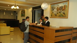 A reception desk with a wooden finish and black accents, a yellow sofa, and a painting of horses on the wall. - Hotel Unik (Bandung)