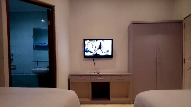 A hotel room with two beds, a TV on the wall, a bathroom visible through a glass door, and a wardrobe. - Hotel Unik (Bandung)