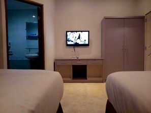 A hotel room with two beds, a TV on the wall, a bathroom visible through a glass door, and a wardrobe. - Hotel Unik (Bandung)