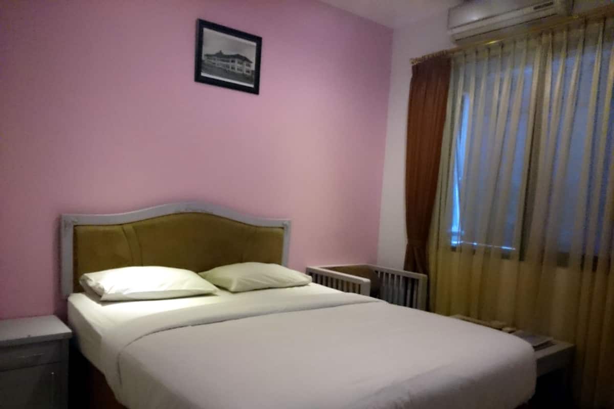 A single bed with a headboard, a bedside table, and a window with curtains.