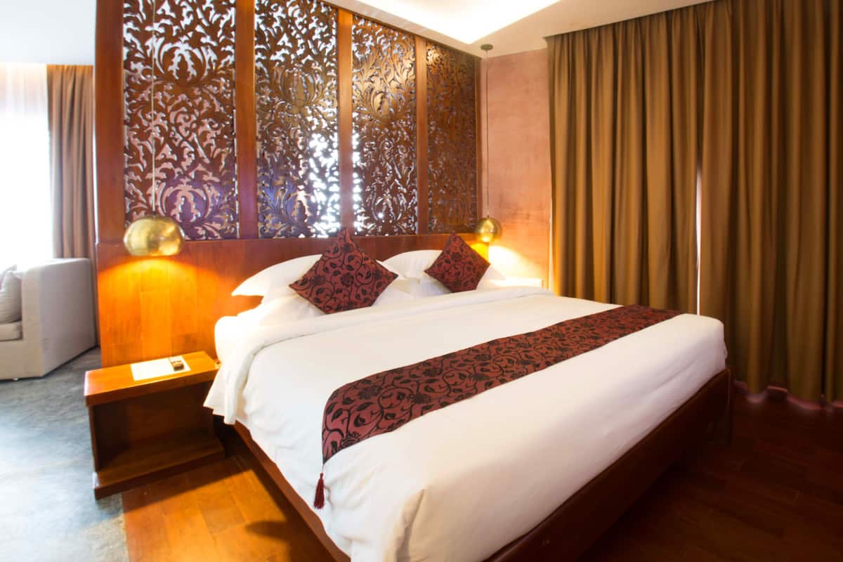 Een hotelkamer met een groot bed, een houten hoofdeinde en een decoratieve scheidingswand.