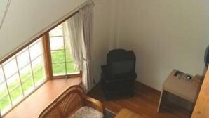 Een kamer met een houten bank, een klein tafeltje, een zwarte kast en een raam met gordijnen.