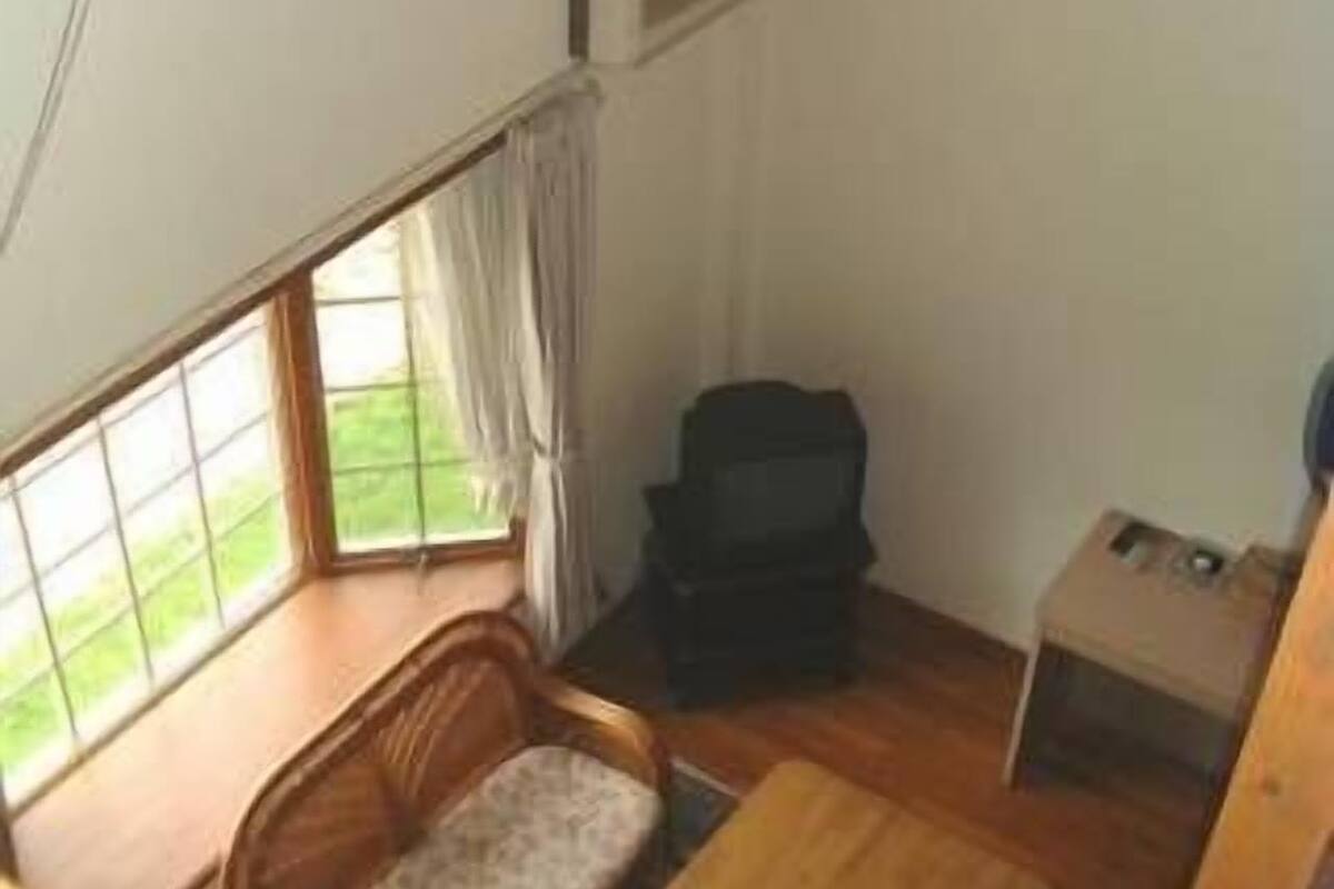 Une pièce avec un canapé en bois, une petite table, un meuble noir et une fenêtre avec des rideaux.