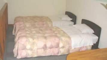 A small, single-room accommodation with a bed, a bedside table, and a chair.