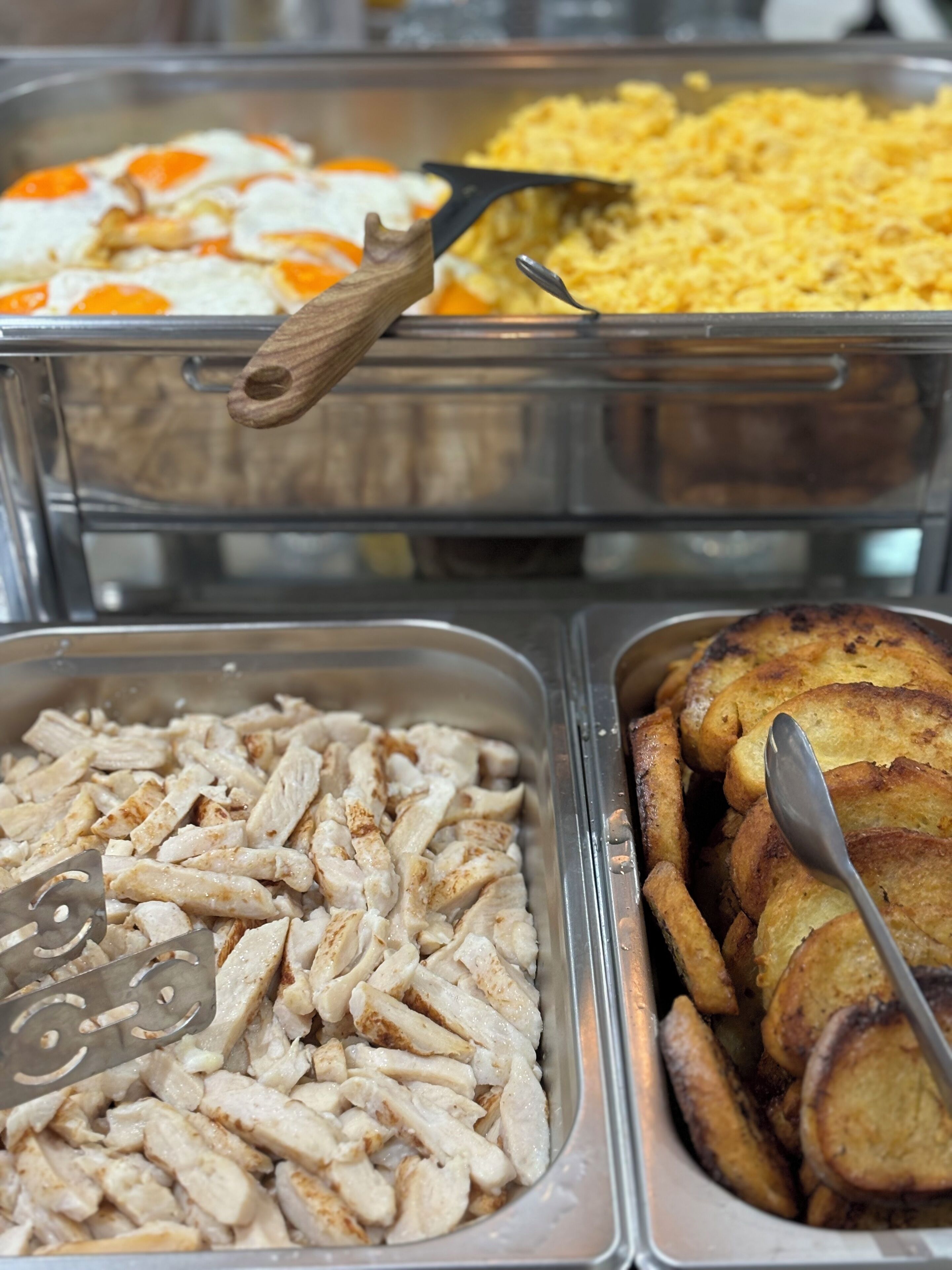 A buffet with various food options including sliced chicken, fried eggs, and potato wedges.
