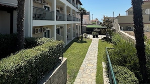A multi-story building with balconies, a stone pathway, and palm trees. - Samel Hotel (Kassandra)