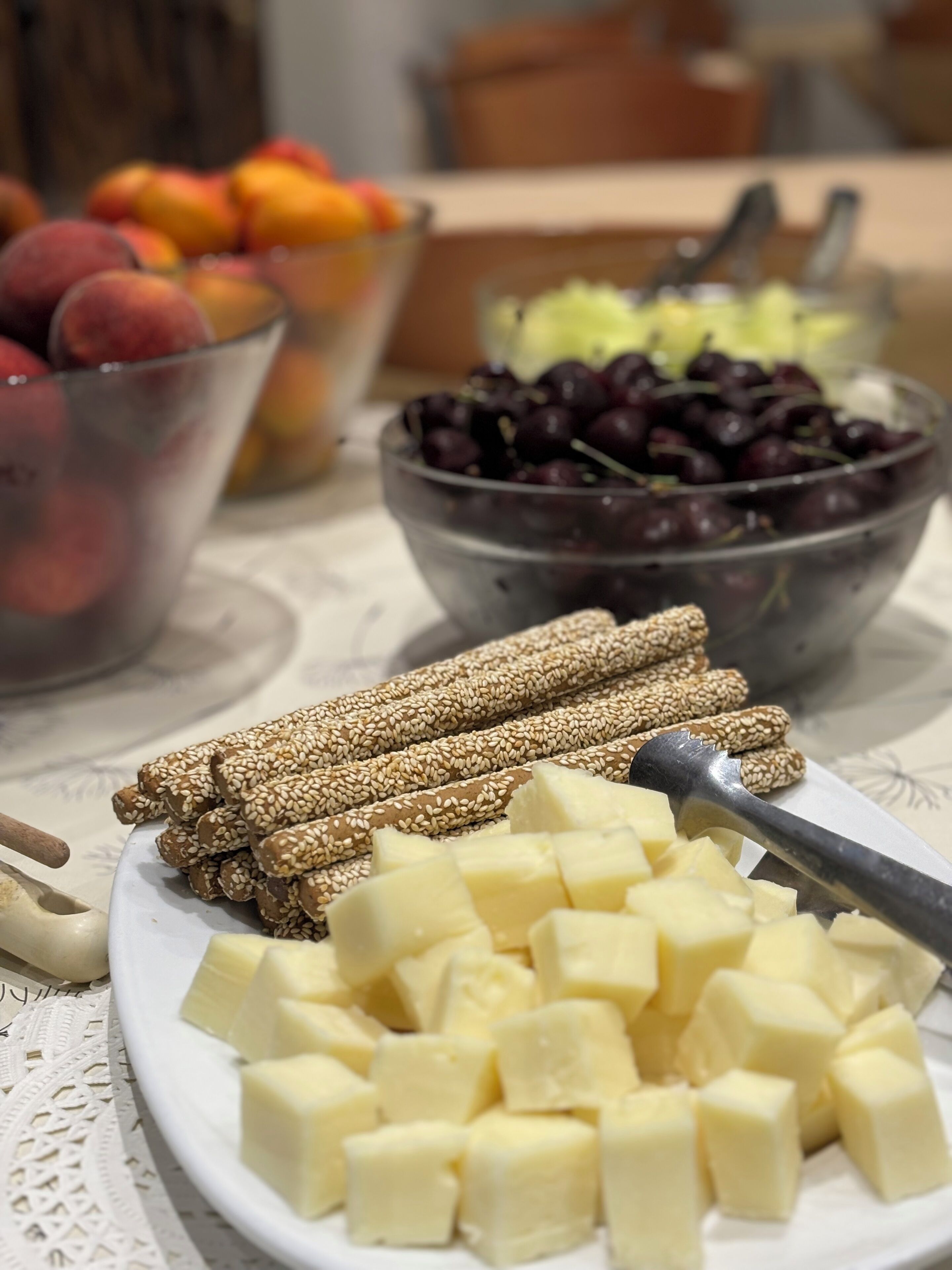 A table with various food items including a bowl of cherries, a bowl of grapes, and a plate of cheese cubes.