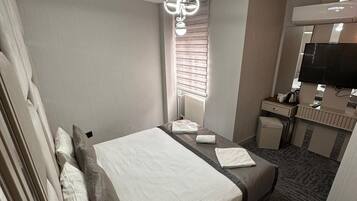 A hotel room with a bed, bedside tables, a desk, a mirror, and a television.